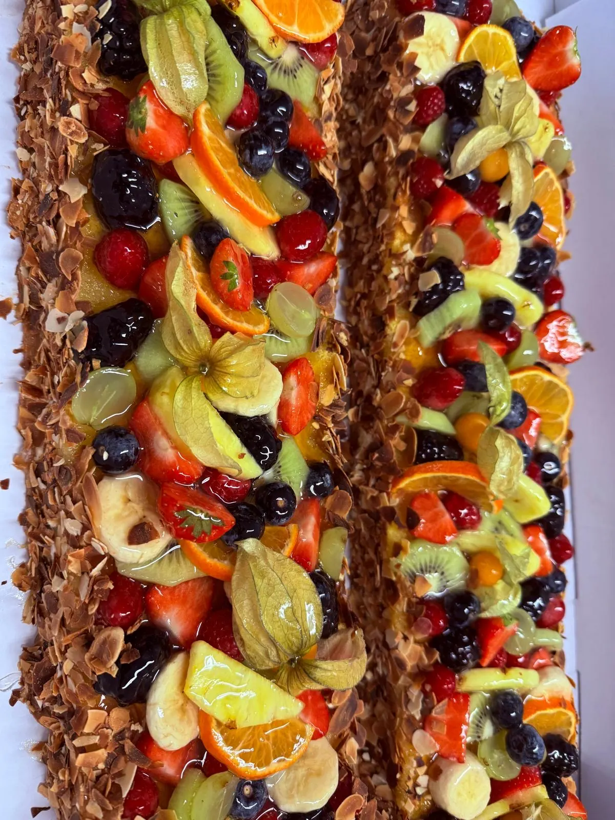 Zwei Obstschnitten vom Blech mit Beeren, Kiwi, Orangen und Physalis, am Rand Mandelblättchen