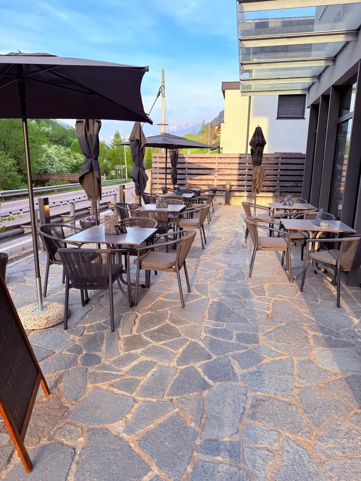 Sonnenterrasse des Cafés mit Tischen, Sonnenschirmen und Bergen