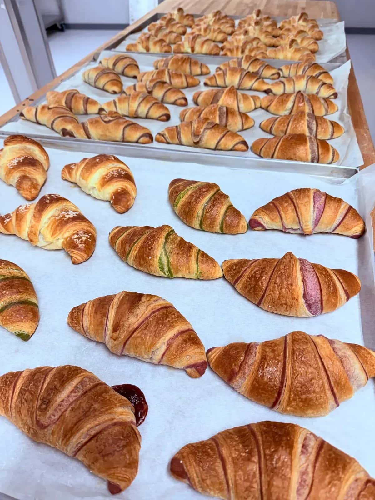 Frische Croissants auf dem Backblech, einige mit grünen und rosa Streifen