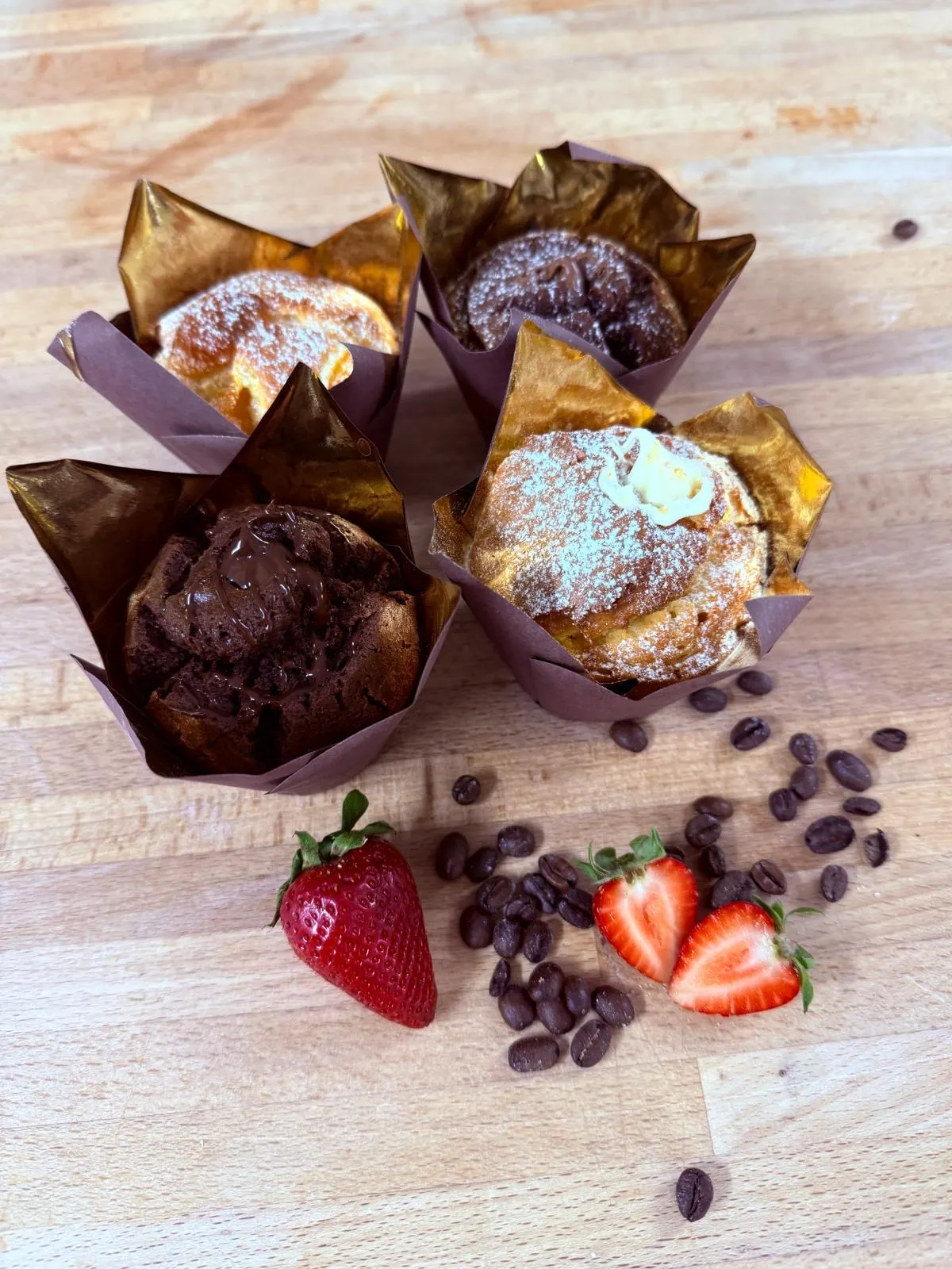 Vier Muffins in goldenen Förmchen, dazu Kaffeebohnen und Erdbeeren