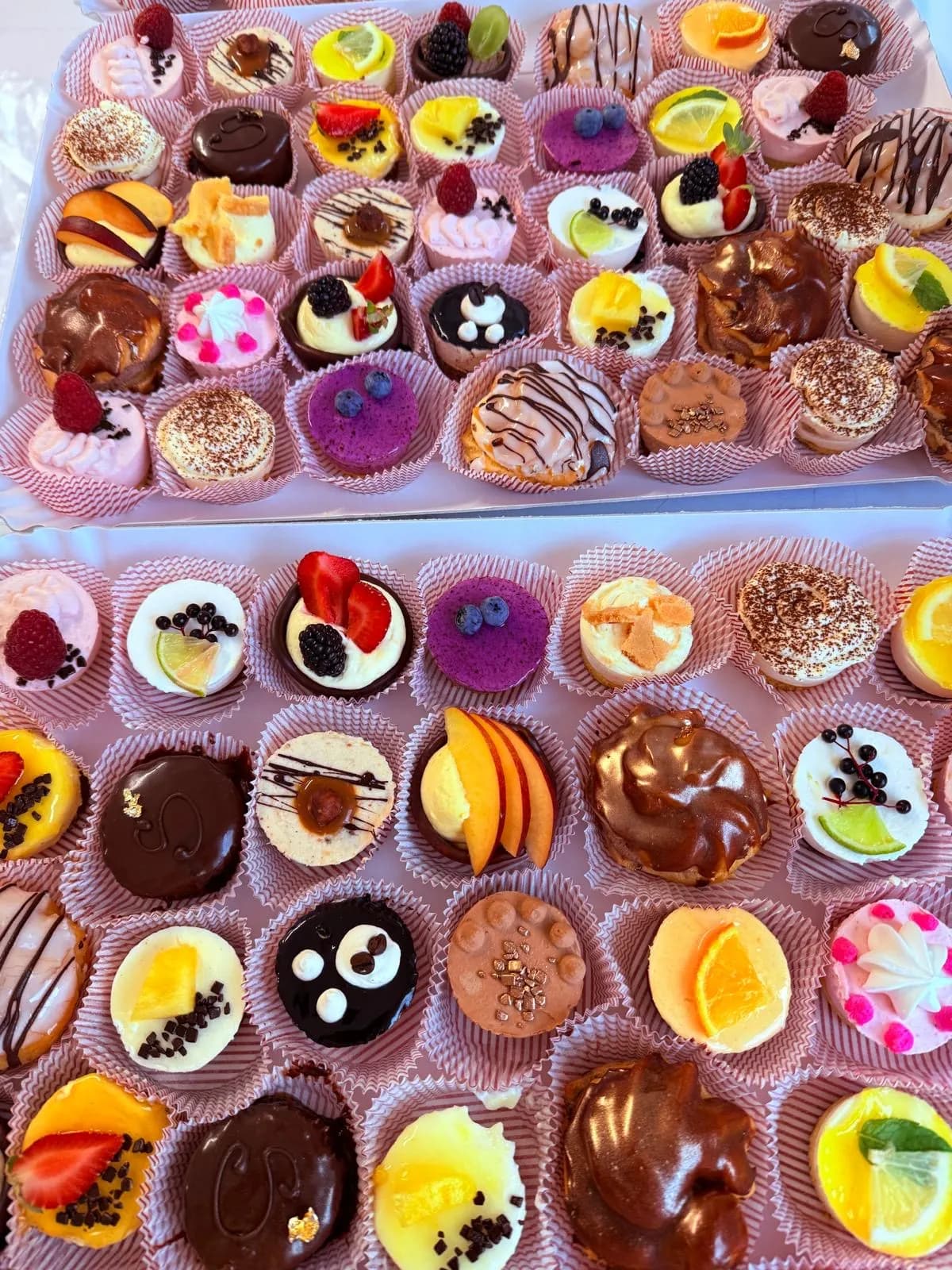 Zwei Tabletts mit bunten Petit Fours in rosa Papierkapseln