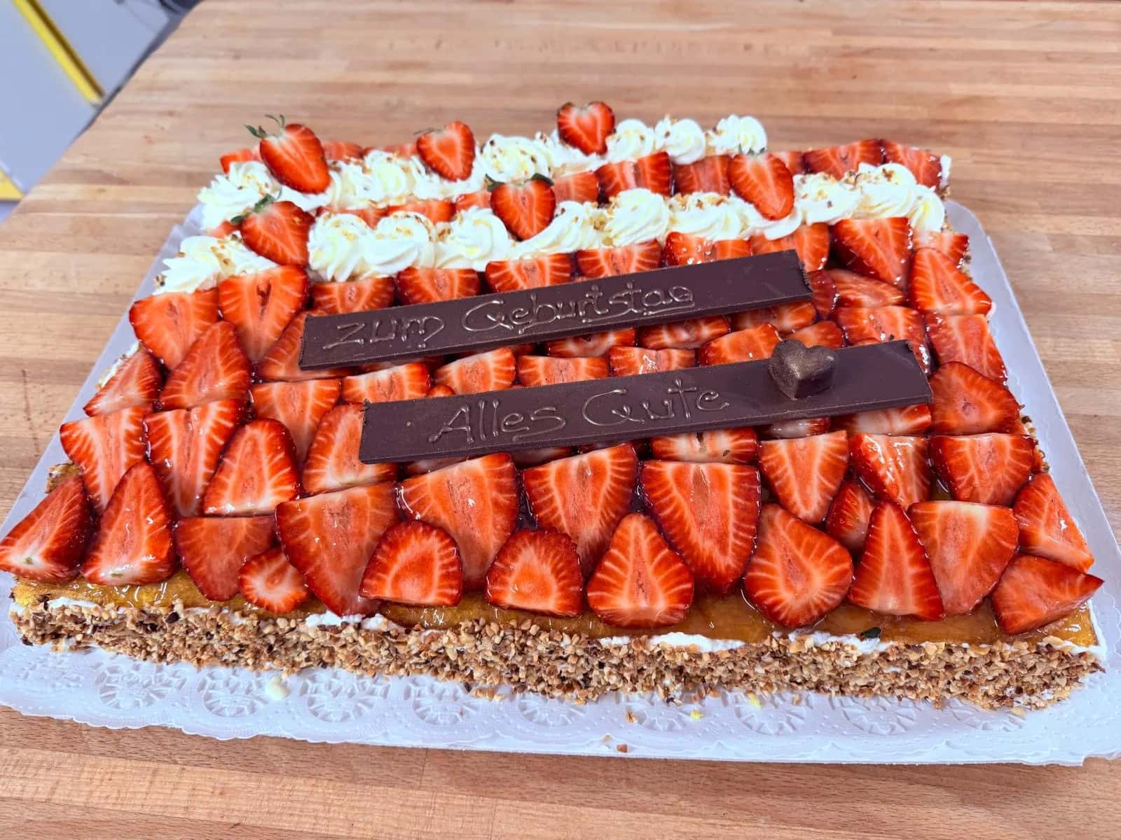 Rechteckige Geburtstagstorte, dicht belegt mit Erdbeeren, darauf zwei Schokoschilder mit „Zum Geburtstag“ und „Alles Gute“