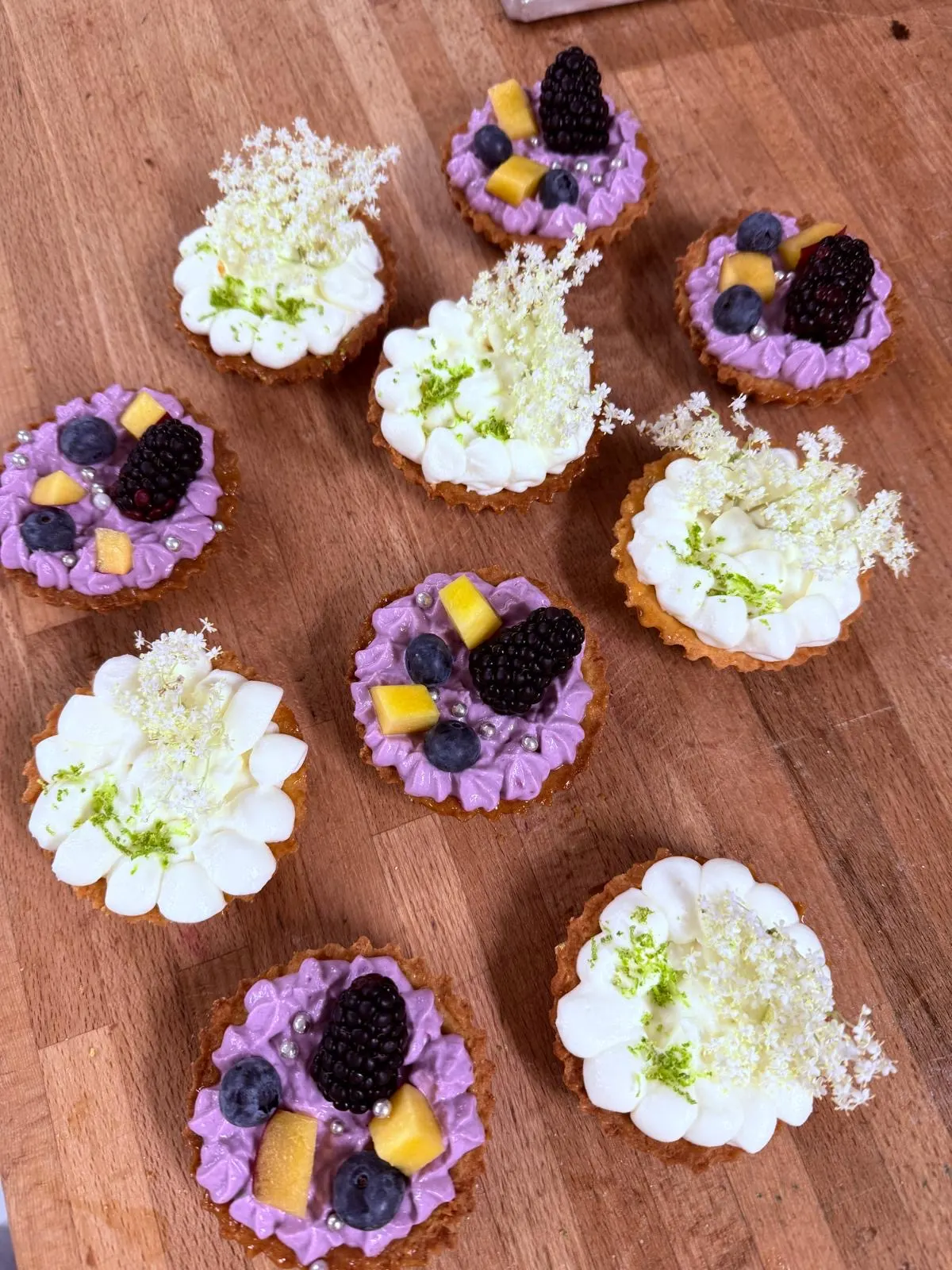 Feine Törtchen mit Holunderblüten, Beerencreme und Brombeeren auf einem Holztisch