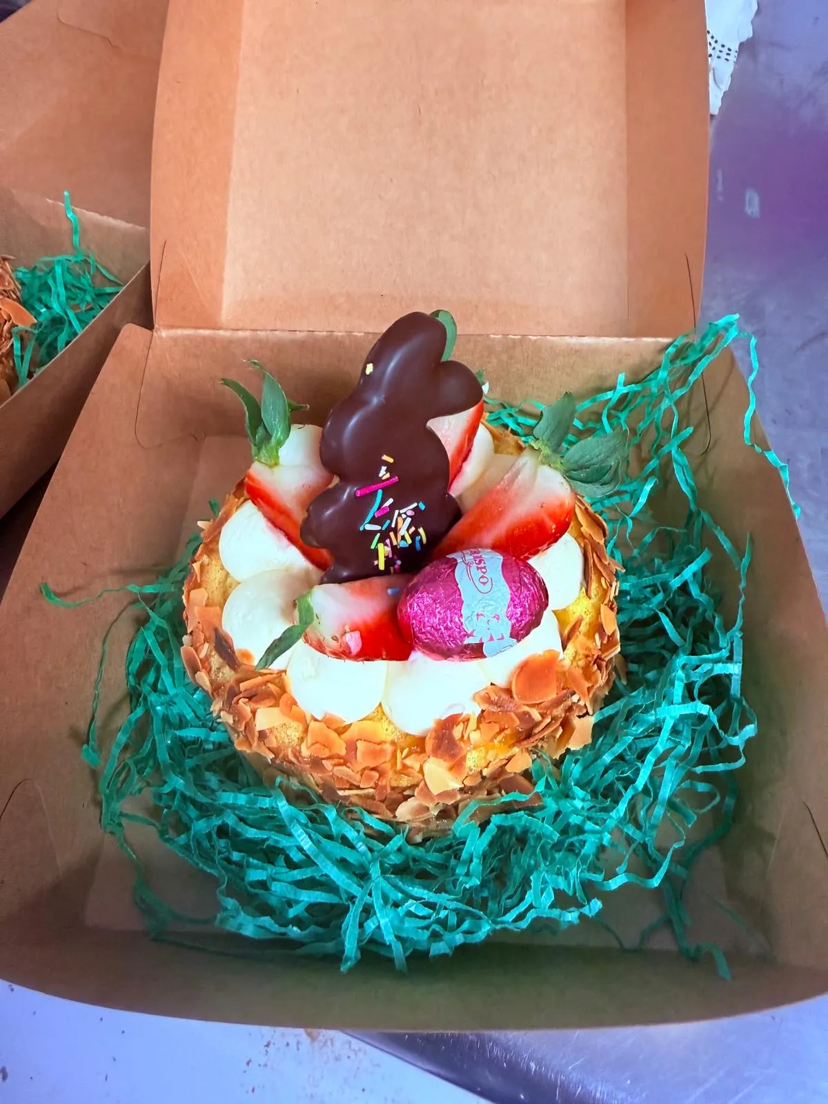 Ostertörtchen mit Schokohase, Erdbeeren und Mandelrand in einer Schachtel mit Ostergras