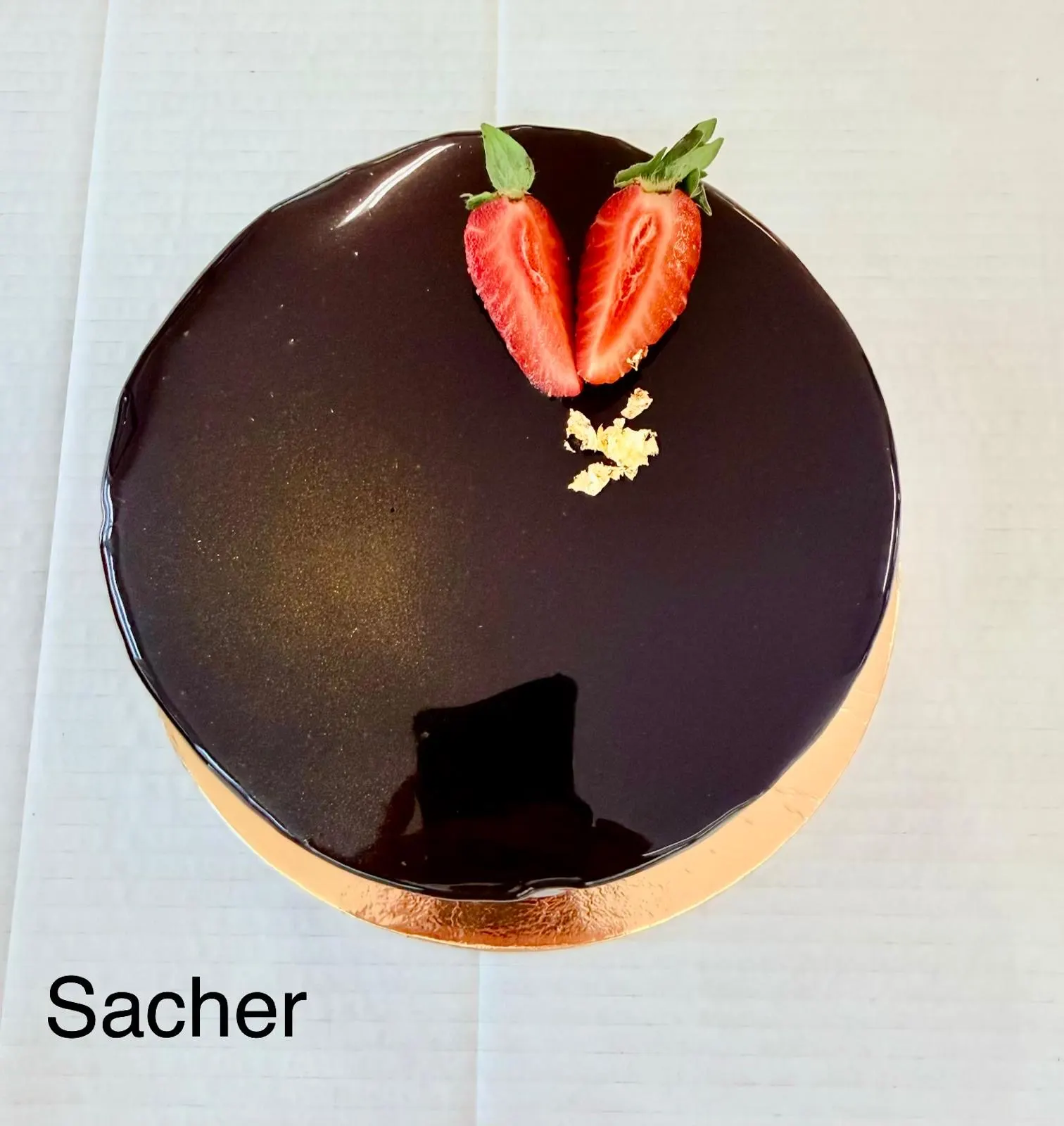 Sachertorte mit glänzender Schokoladenglasur, zwei Erdbeerhälften und Blattgold
