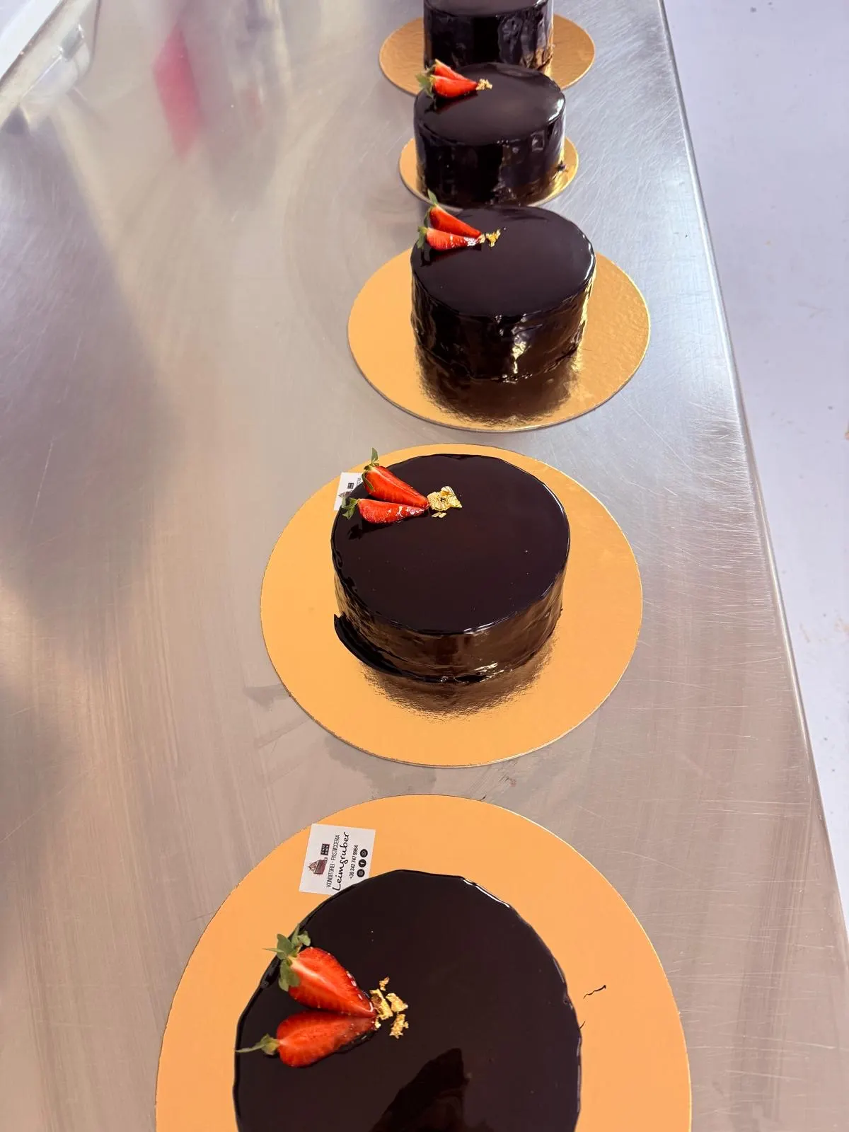 Ganze Sachertorte mit glänzender Spiegelglasur, Erdbeeren und Blattgold auf einer goldenen Tortenplatte