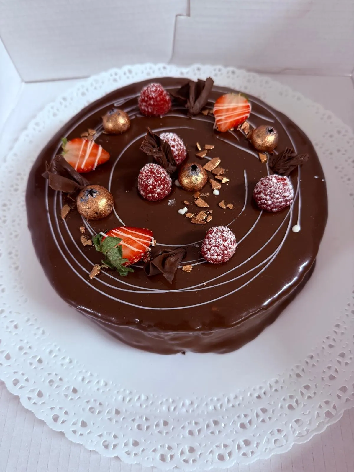 Schokoladentorte mit Glasur, gezuckerten Himbeeren, Erdbeeren und Goldkugeln im Tortenkarton