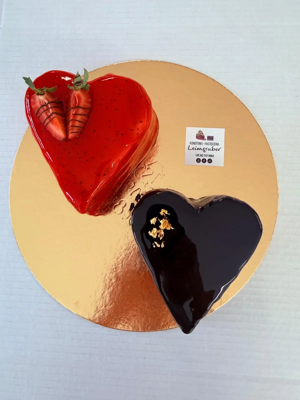 Zwei Herzen mit Spiegelglasur, eines rot mit Erdbeeren, eines dunkel mit Blattgold